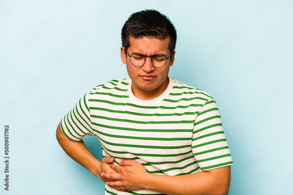 Young hispanic man isolated on blue background having a liver pain, stomach ache. Young hispanic man isolated on blue background having a liver pain, stomach ache.