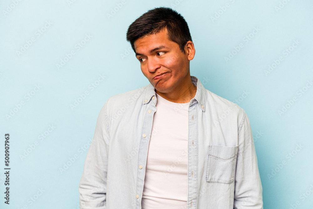 Young hispanic man isolated on blue background shrugs shoulders and open eyes confused. Young hispanic man isolated on blue background shrugs shoulders and open eyes confused.