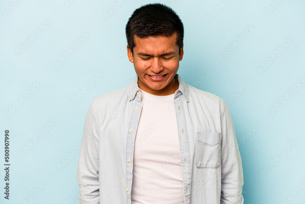 Young hispanic man isolated on blue background laughs and closes eyes, feels relaxed and happy. Young hispanic man isolated on blue background laughs and closes eyes, feels relaxed and happy.