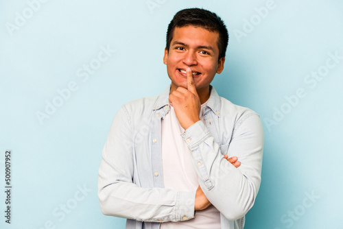 Young hispanic man isolated on blue background smiling happy and confident, touching chin with hand.