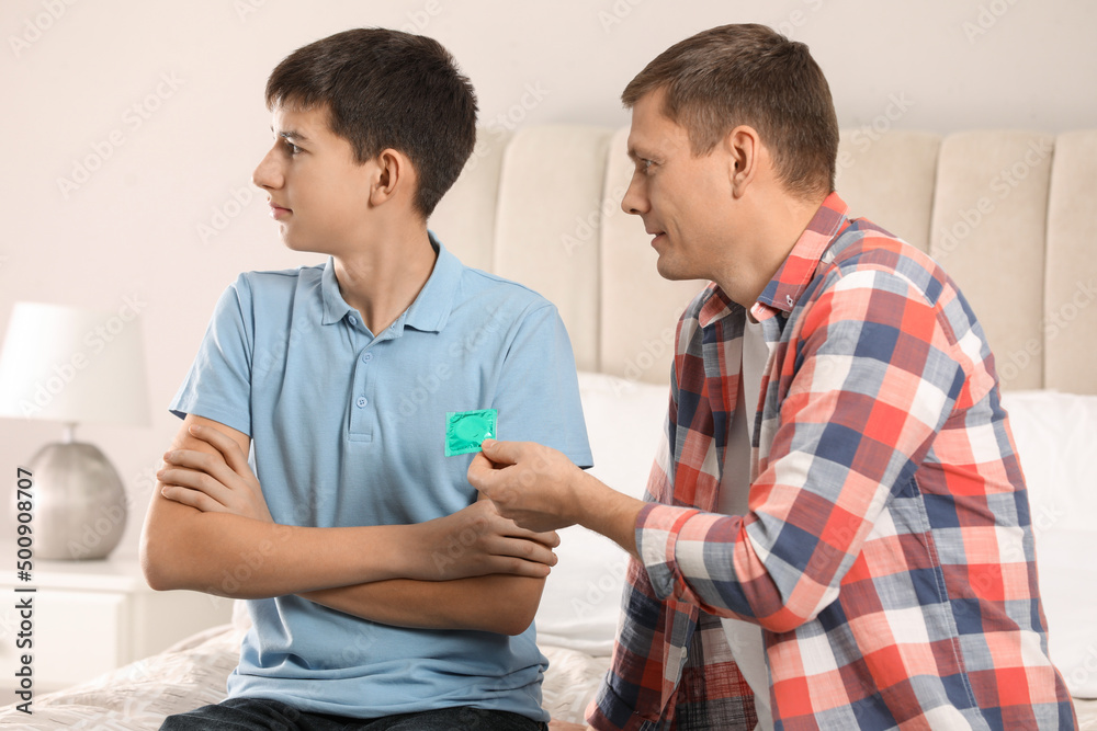 Father giving condom to his teenage son in bedroom. Sex education concept Father giving condom to his teenage son in bedroom. Sex education concept
