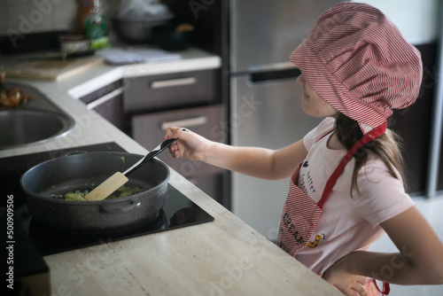 Dziewczynka stoi przed kuchenką i gotuje na patelni 