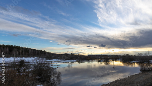 Epic spring landscape by the river. The flood of the river in early spring. A colorful sunset is reflected in the water. March evening landscape.