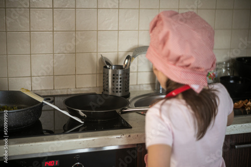 Obraz na płótnie Dziewczynka stoi przed kuchenką i gotuje na patelni w salonie
