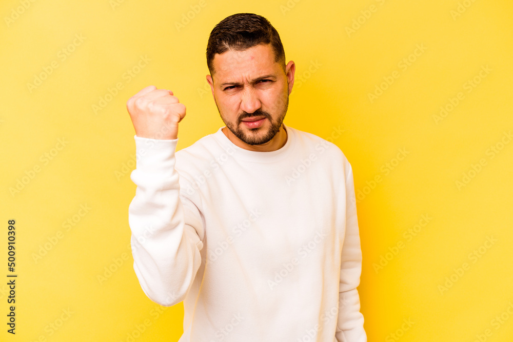 Young hispanic man isolated on yellow background showing fist to camera, aggressive facial expression. Young hispanic man isolated on yellow background showing fist to camera, aggressive facial expression.
