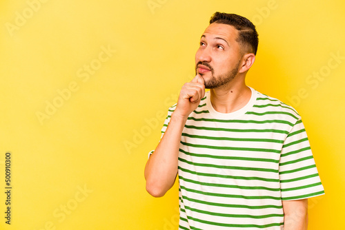 Young hispanic man isolated on yellow background looking sideways with doubtful and skeptical expression.