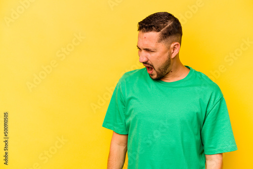 Young hispanic man isolated on yellow background shouting very angry, rage concept, frustrated.