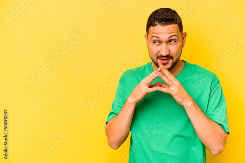 Young hispanic man isolated on yellow background making up plan in mind, setting up an idea.