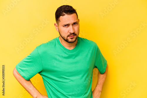 Young hispanic man isolated on yellow background frowning face in displeasure, keeps arms folded.