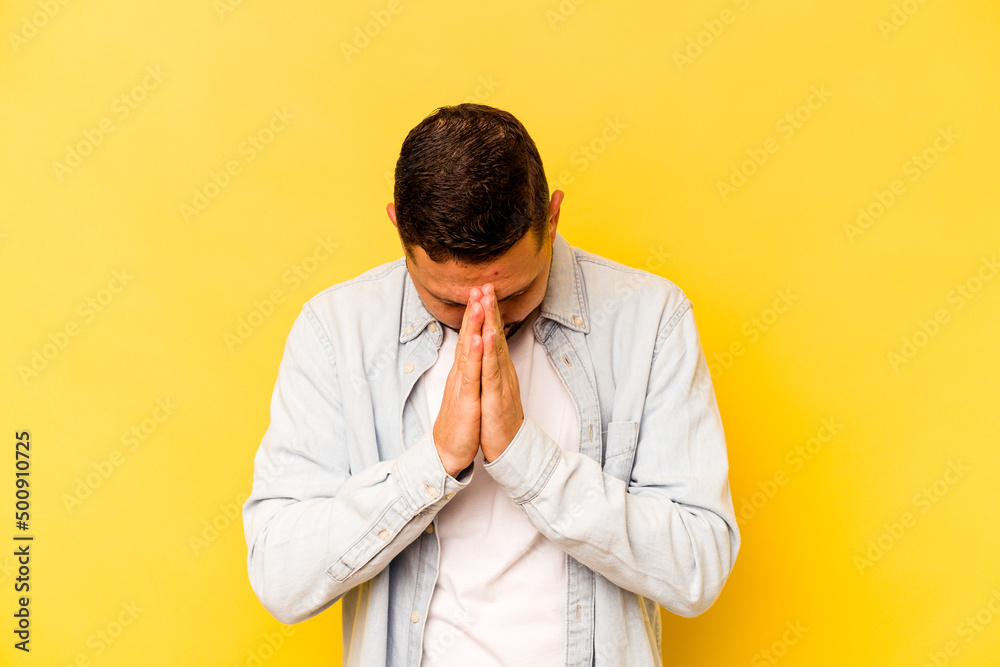 Young hispanic man isolated on yellow background praying, showing devotion, religious person looking for divine inspiration. Young hispanic man isolated on yellow background praying, showing devotion, religious person looking for divine inspiration.