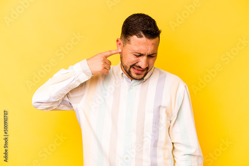 Young hispanic man isolated on yellow background covering ears with hands.