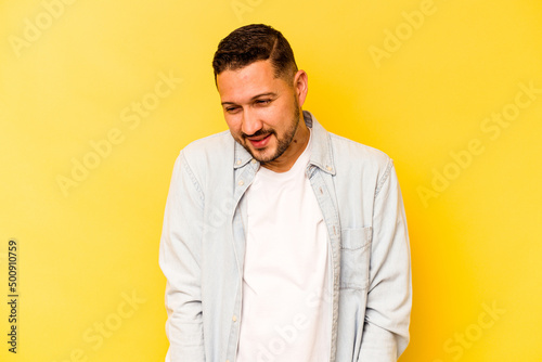 Young hispanic man isolated on yellow background laughs and closes eyes, feels relaxed and happy.