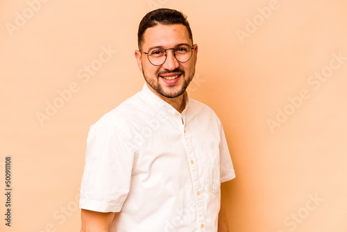 Young hispanic man isolated on beige background confident keeping hands on hips. © Asier