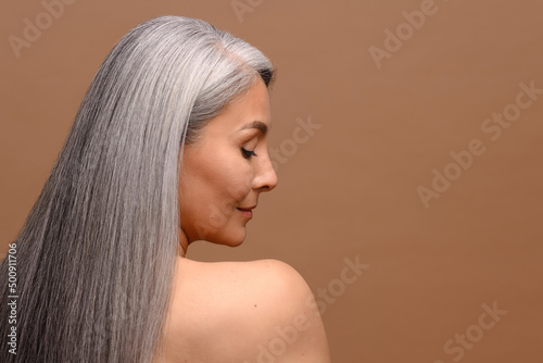 Obraz na plátně Charming good-looking Asian middle-aged woman with naked shoulders, looks down isolated beige background