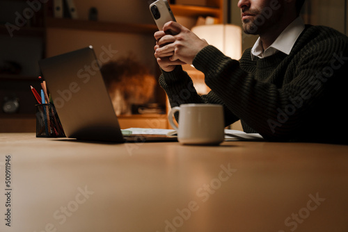 Young beard man using mobile phone while working with laptop
