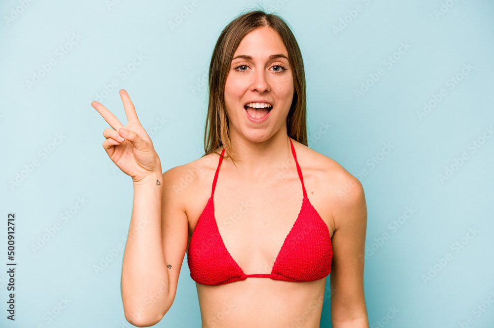 Young caucasian woman going to the beach isolated on blue background joyful and carefree showing a peace symbol with fingers.
