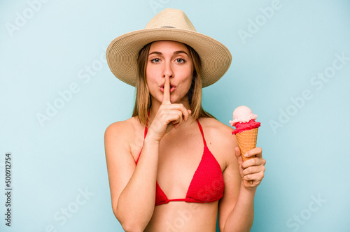 Young caucasian woman wearing a bikini and holding an ice cream isolated on blue background keeping a secret or asking for silence.