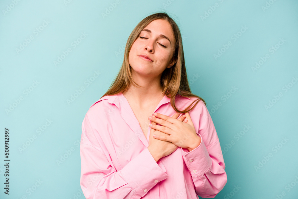 Young caucasian woman isolated on blue background has friendly expression, pressing palm to chest. Love concept. Young caucasian woman isolated on blue background has friendly expression, pressing palm to chest. Love concept.