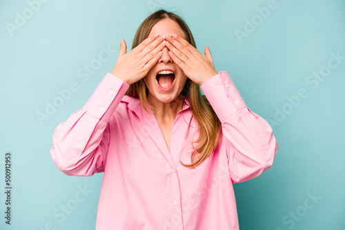 Young caucasian woman isolated on blue background covers eyes with hands, smiles broadly waiting for a surprise.