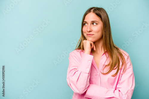 Young caucasian woman isolated on blue background relaxed thinking about something looking at a copy space.