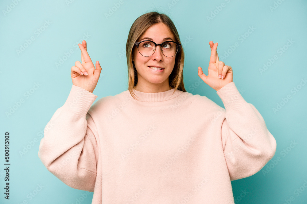 Young caucasian woman isolated on blue background crossing fingers for having luck Young caucasian woman isolated on blue background crossing fingers for having luck