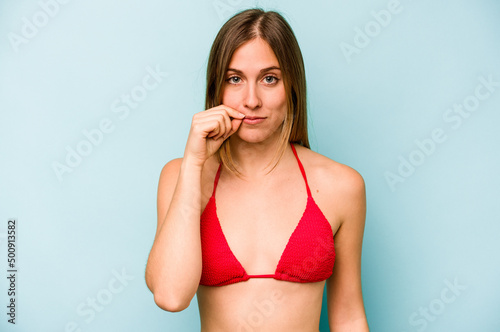 Young caucasian woman going to the beach isolated on blue background with fingers on lips keeping a secret.