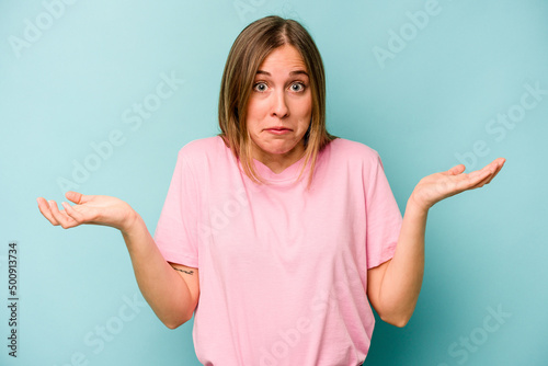 Foto Young caucasian woman isolated on blue background doubting and shrugging shoulders in questioning gesture