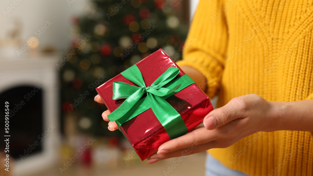 Woman with beautifully wrapped Christmas gift indoors, closeup Woman with beautifully wrapped Christmas gift indoors, closeup