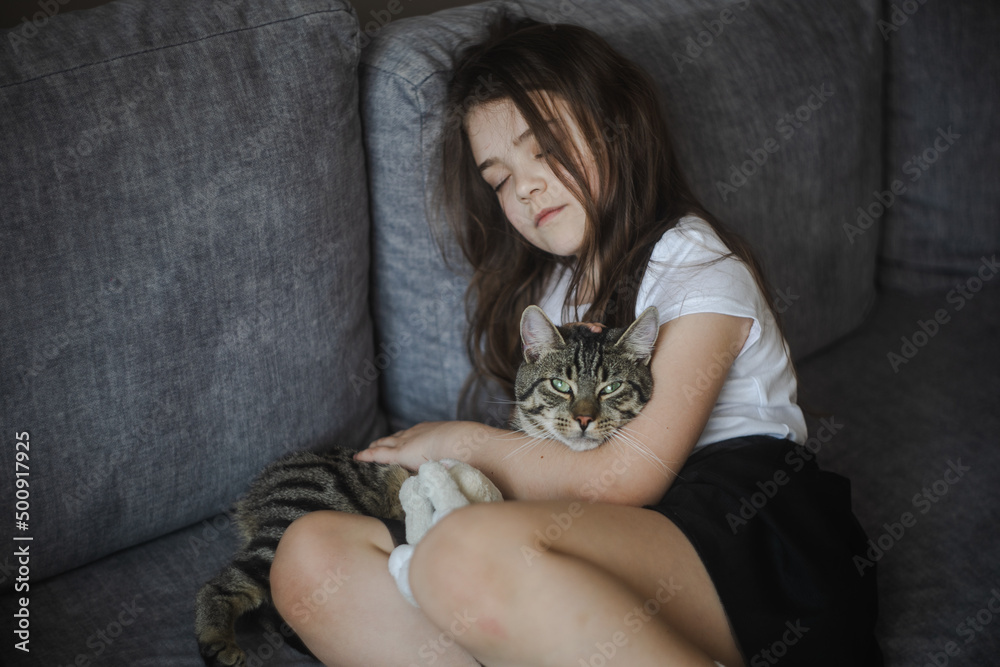 Młoda dziewczynka odpoczywająca z kotem na sofie - obrazy, fototapety, plakaty 