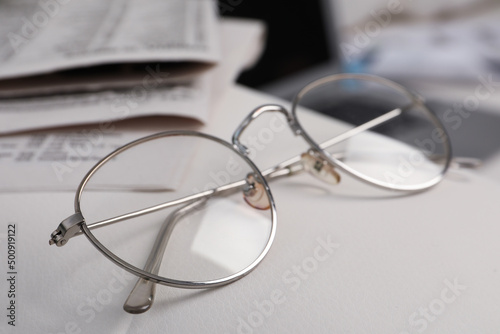 Glasses and newspapers on armrest indoors, closeup © New Africa