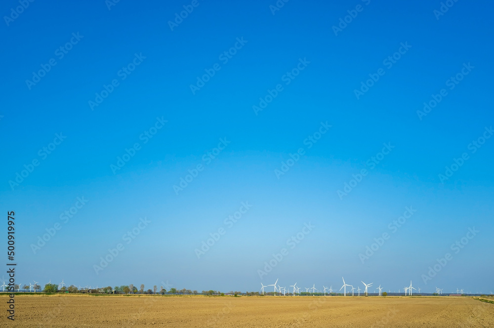 Agricultural land, plowed field, against the blue sky and wind turbines. Wonderful rural landscape, on spring day.
