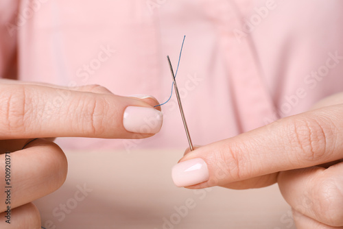 Woman threading sewing needle at table, closeup