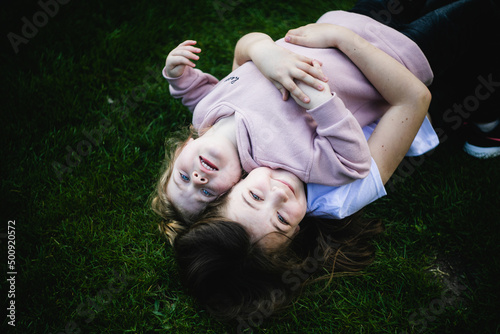 Dwie siostry przytulają się i leżą plecami na zielonej trawie