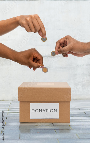 charity, financial support and saving concept - close up of hands putting coins into donation box over urban steet background photo