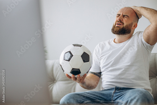 Man holding football ball and watching soccer online at home