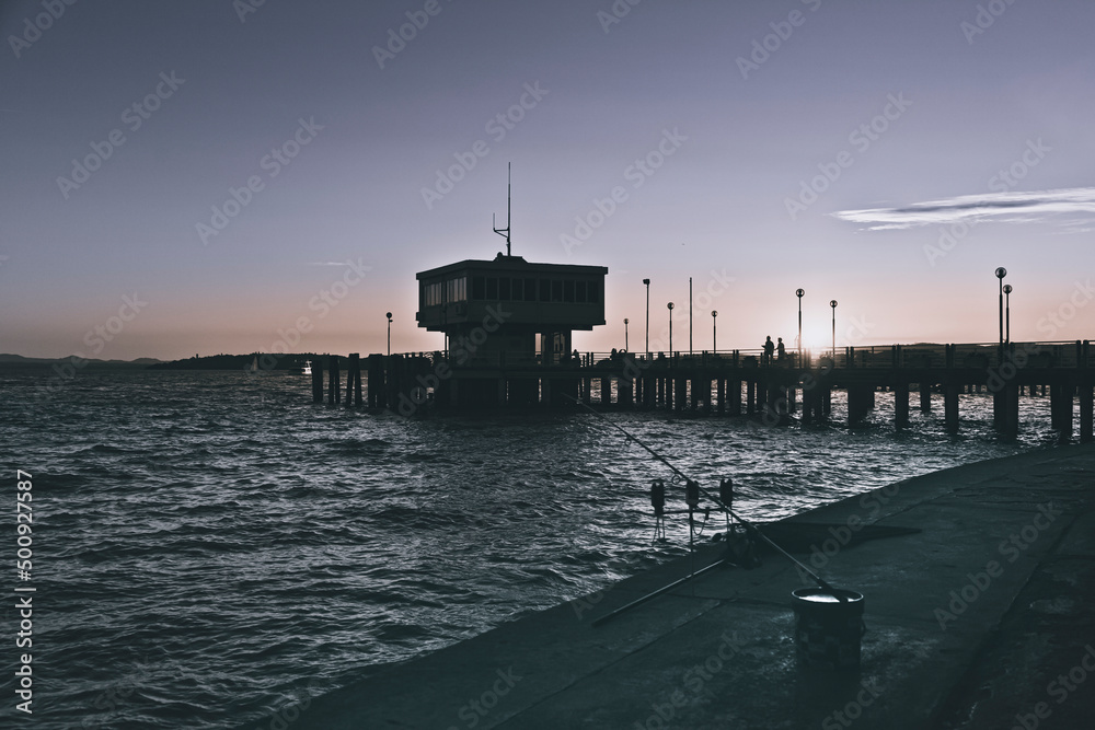 Silhouette of two people walking on the pier of a lake at sunset Silhouette of two people walking on the pier of a lake at sunset