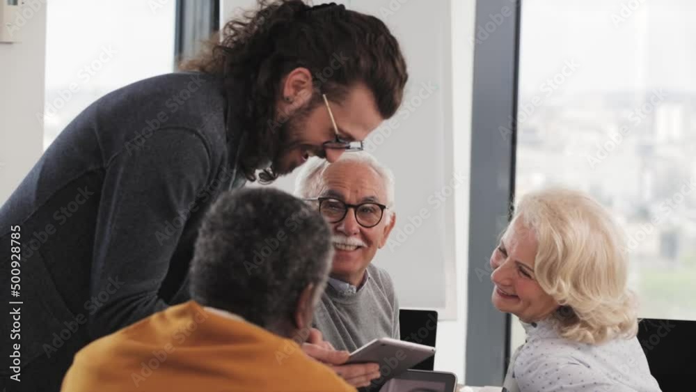 Young hipster educator teaching group of senior multiracial people using technology and the internet in the classroom. Young hipster educator teaching group of senior multiracial people using technology and the internet in the classroom.