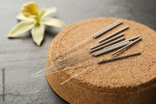Cork coaster with acupuncture needles on black table, closeup
