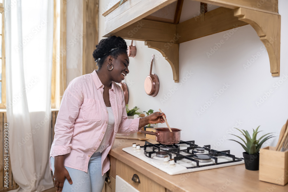 Contented african woman in pink clothes cooking in the kitchen Contented african woman in pink clothes cooking in the kitchen