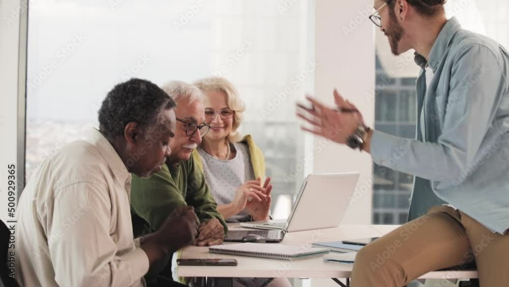 A multicultural group of elderly students discusses an assignment with their young educator in the classroom. A multicultural group of elderly students discusses an assignment with their young educator in the classroom.