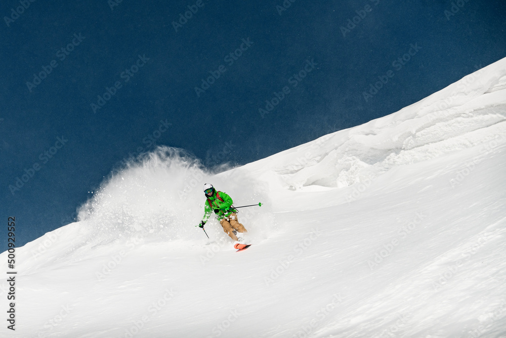 skier descending a snow-covered mountain slope and splash of snow behind him