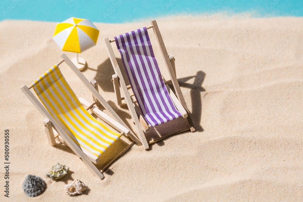 A toy beach chaise longue, seashells, a starfish on white sand with shadows. Sunlight. The concept of the sea, a beach holiday and a resort. Summer minimalism.