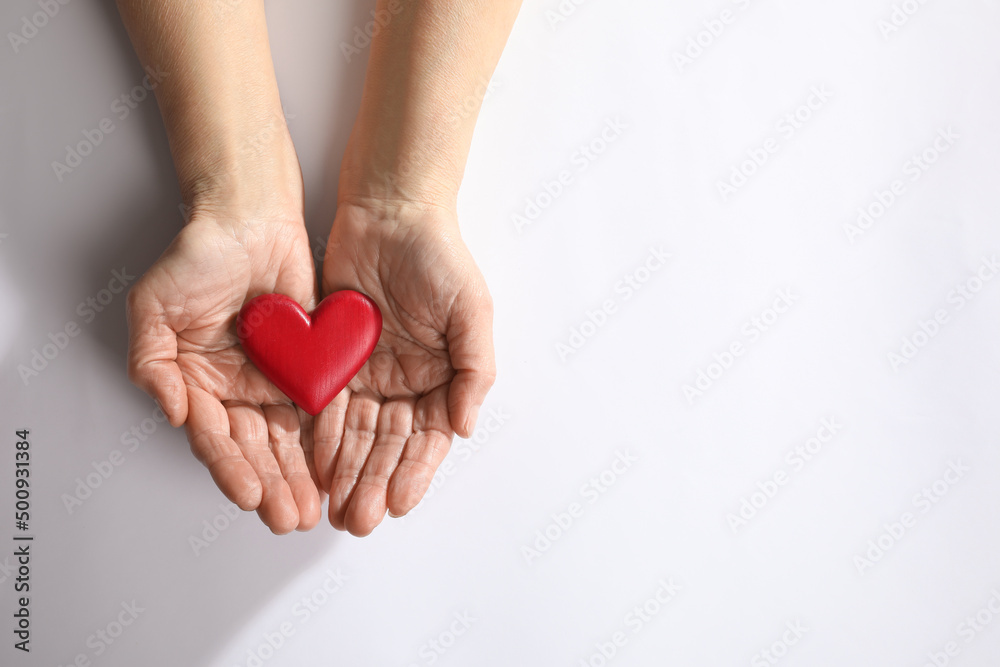Obraz premium Elderly woman holding red heart in hands on white background, top view