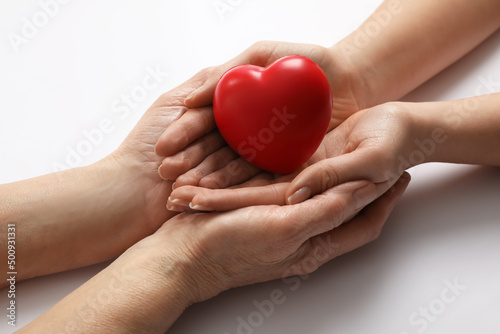 Young and elderly women holding red heart on white background, closeup