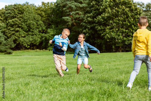 childhood, leisure and people concept - group of happy kids playing tag game and running at park