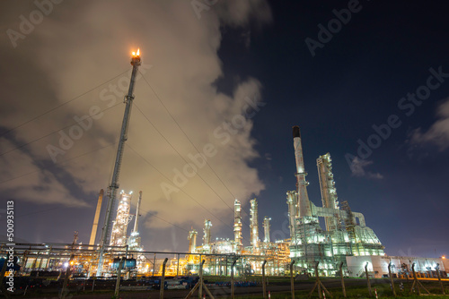 Oil​ refinery​ and tower flare fire of petrochemistry industry in oil​ and​ gas​ ​industry with​ cloud​ blue​ ​sky traffic light road transportation truck