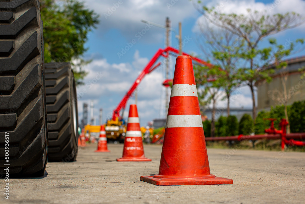 Orange traffic cone in parking lot near hydraulic crane Orange traffic cone in parking lot near hydraulic crane