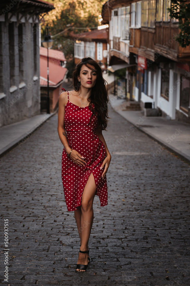 beautiful brunette girl in a red dress walks along the cobblestones in a beautiful old European town