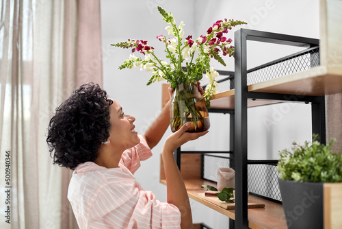 home improvement, decoration and people concept - happy smiling woman placing flowers to shelf #500940346