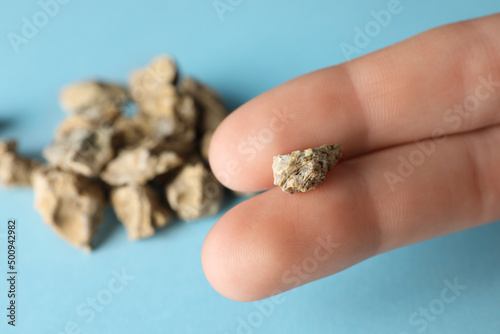 Woman holding kidney stone above light blue background, closeup. Space for text photo